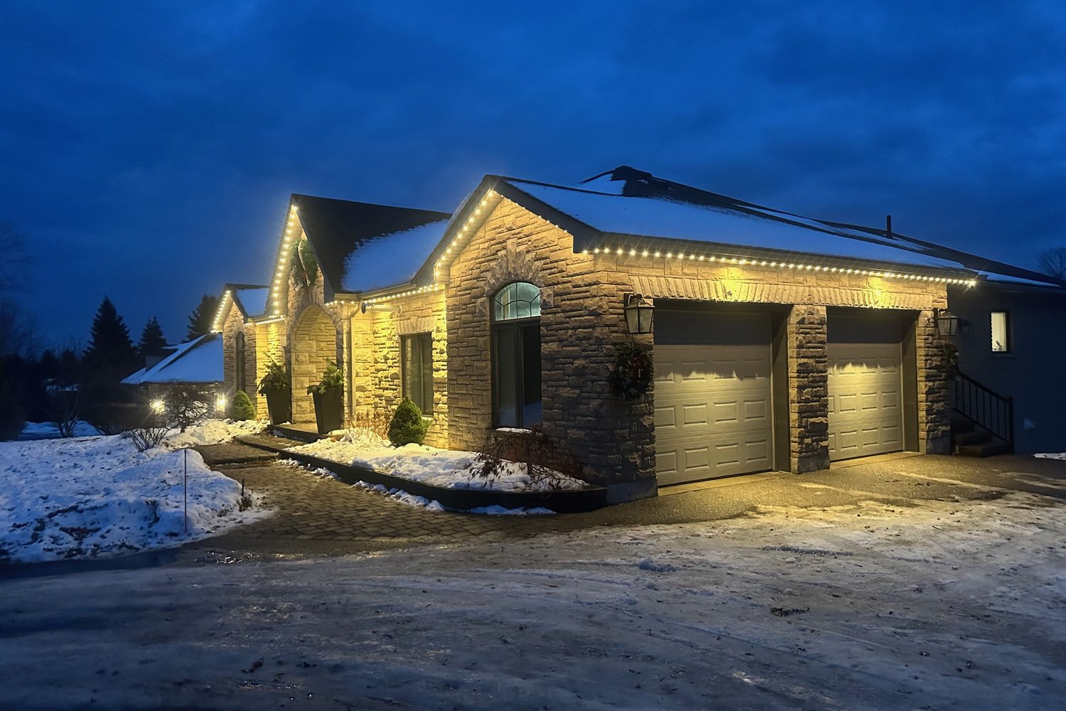 Stone bungalow with warm-white permanent roofline lighting installed by JD Home Solutions